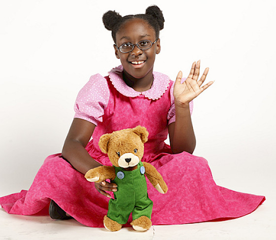 Photo of a young girl wearing a pink dress holding a Corduroy teddy bear.