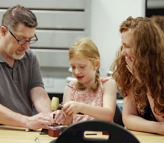 Photo of a man, woman, and young girl working on a metal art project in an art studio at the Windgate Art School.