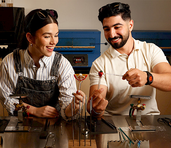 Photo of a man and a woman in an art studio inspecting small glass pieces on rods.