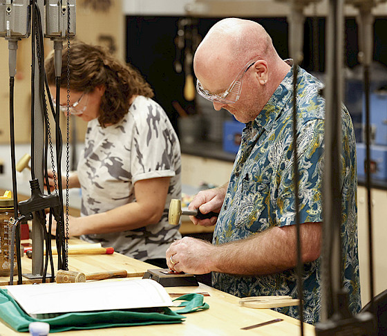 Photo of a man and a woman hammering metal in an art studio at AMFA.