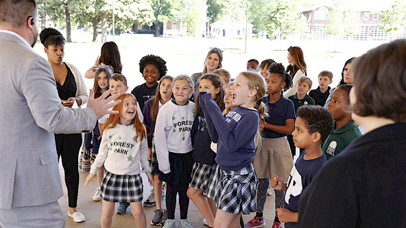 Photo of school children wearing uniforms and smiling in reaction to an animated tour guide.