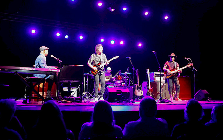 Photo of a band performing on a stage lit with purple lights.