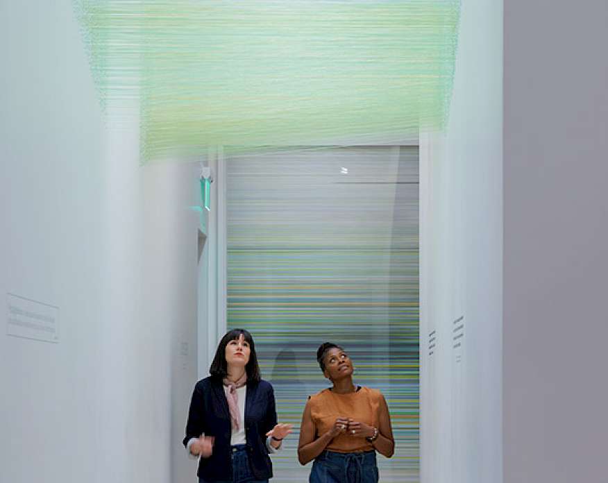 Photo of two women walking underneath a green string art installation in an art gallery.