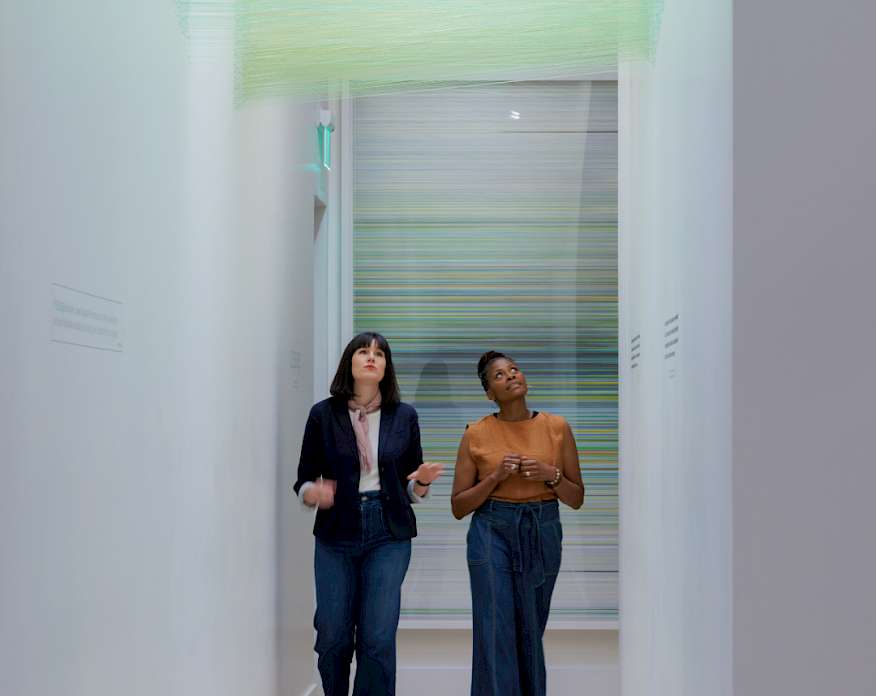 Photo of two women walking underneath a green string art installation in an art gallery.