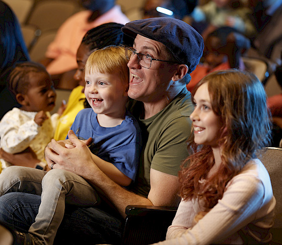 Photo of young children and families smiling while seated in a theater.