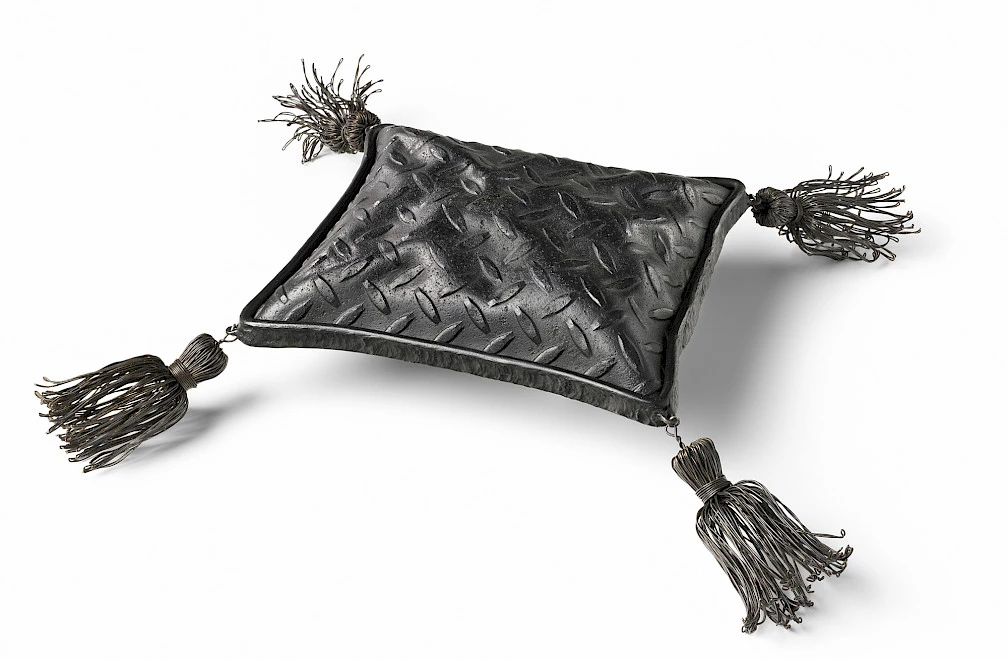 Photo of a fabricated black steel sculpture in the shape of a rectangular pillow with tassels hanging off the four corners.