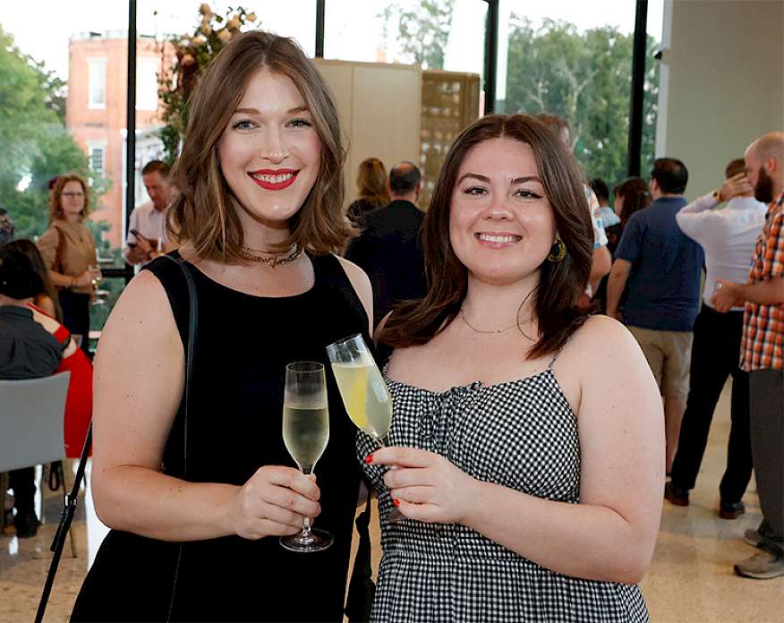 Photo of two women posed smiling and holding cocktails at a party.