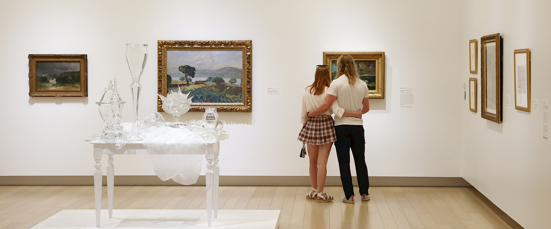 Photo of a couple with their armas around each other looking at a painting in an art gallery.