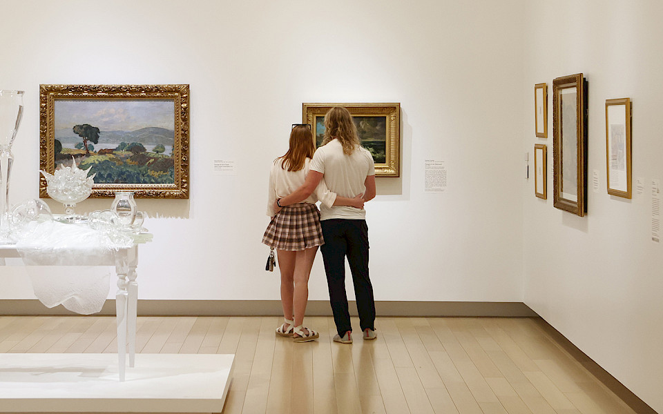 Photo of a couple with their armas around each other looking at a painting in an art gallery.