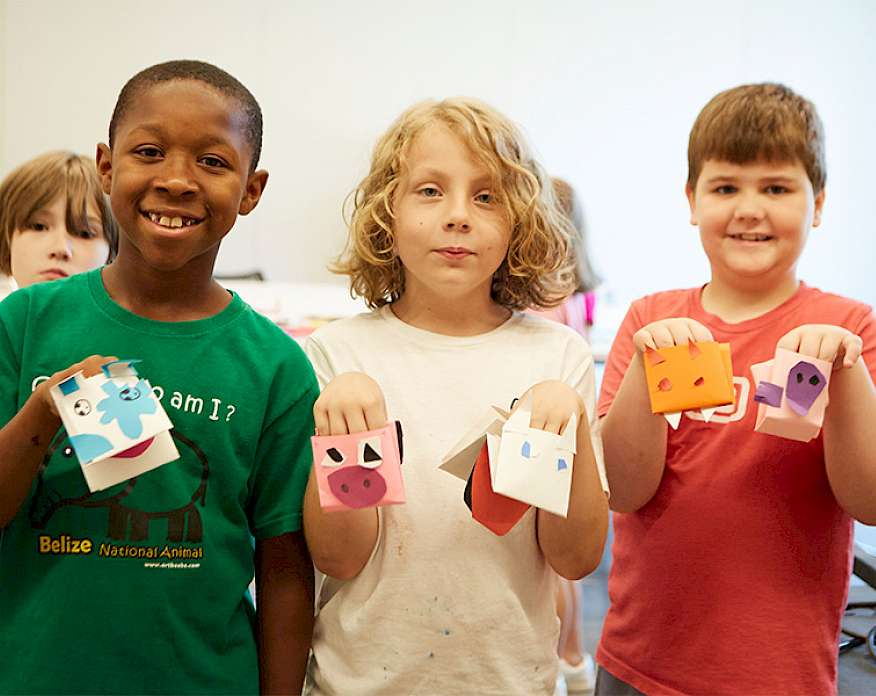 Photo of three young boys smilng and holding handmade paper puppets.