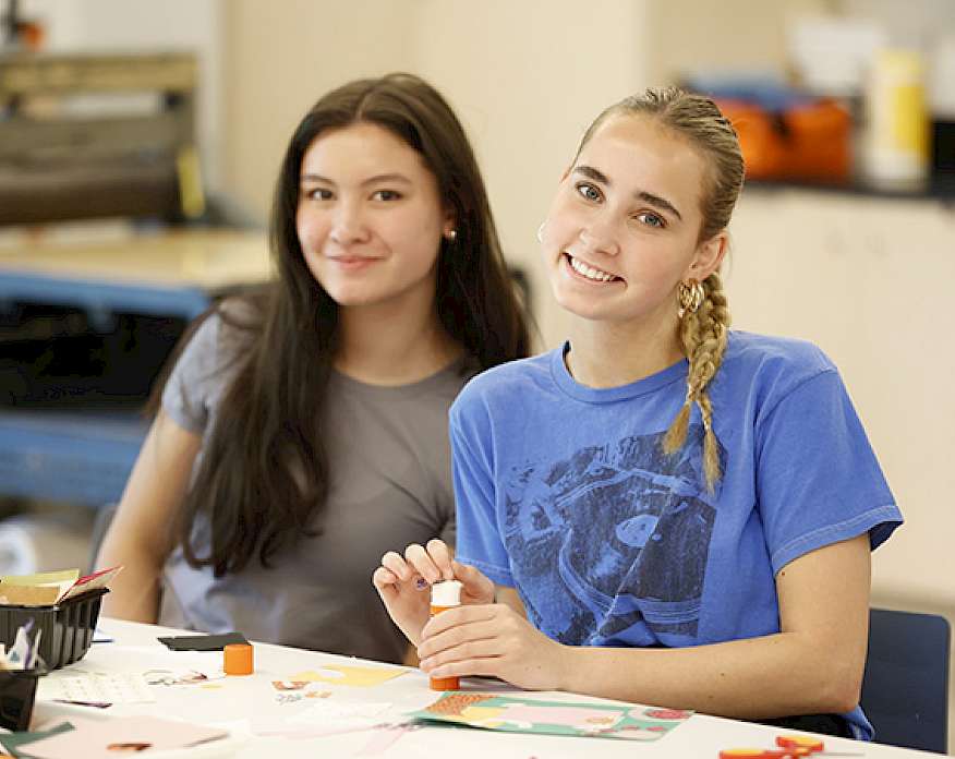 Photo of two teenage girls smiling while working on an art project.