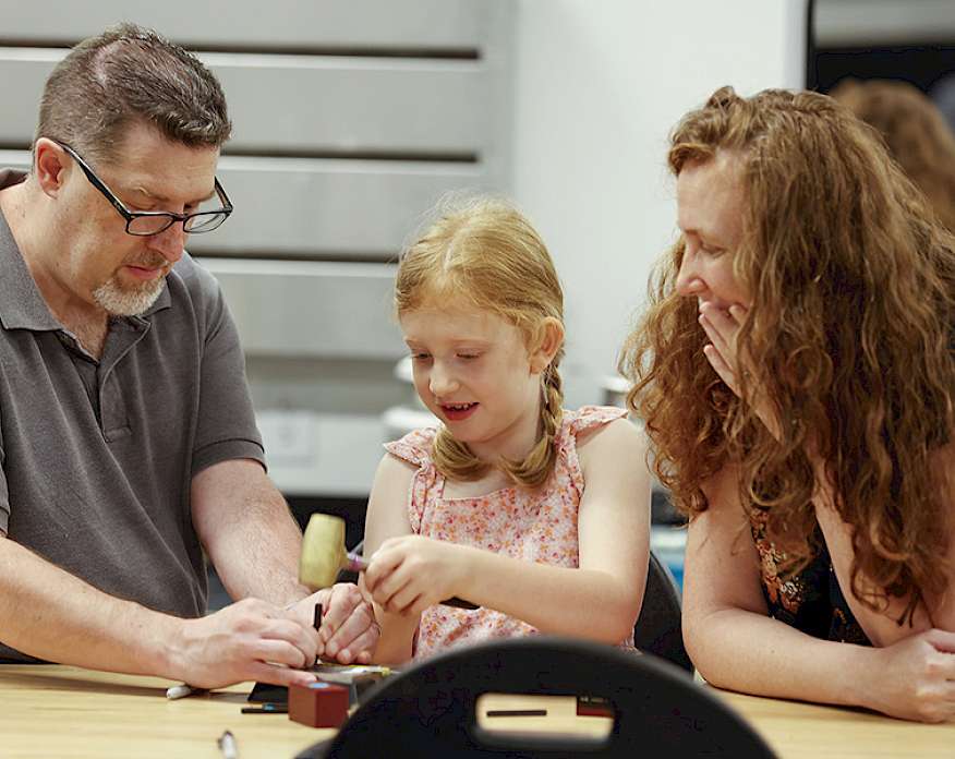 Photo of a man, woman, and young girl working on a metal art project in an art studio at the Windgate Art School
