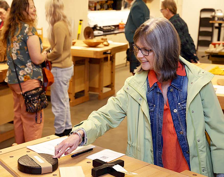 Photo of a woman looking at handmade wooden objects on a table in a wood shop at the Arkansas Museum of Fine Arts.