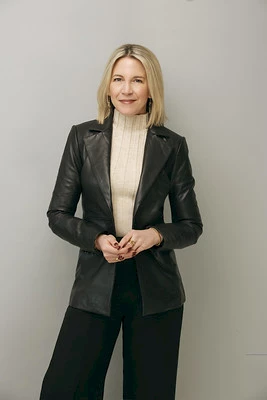 Photo of Malina Tabor wearing black pants, a cream turtleneck sweater, and black leather jacket standing in front of a light gray background.
