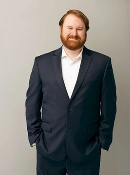 Photo of Spencer Jansen wearing a black suit and white shirt standing in front of a light gray backdrop.