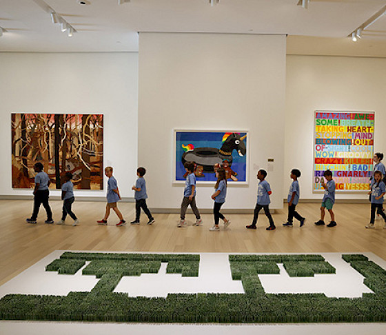 Photo of a line of school children walking through an art gallery with a teacher.