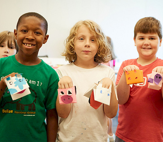 Photo of three young boys smiling and holding handmade animal puppets.