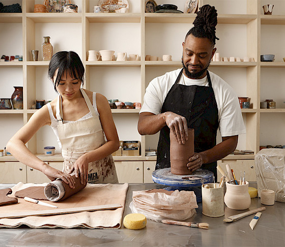 Photo of a woman and a man hand building vases with brown clay in an art studio.