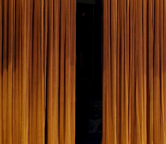 Photo of golden velvet theater curtains partially open on a dark stage.
