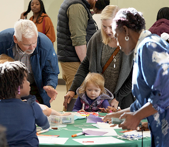 Photo of small children, parents, and grandparents gathered around a table doing crafts.