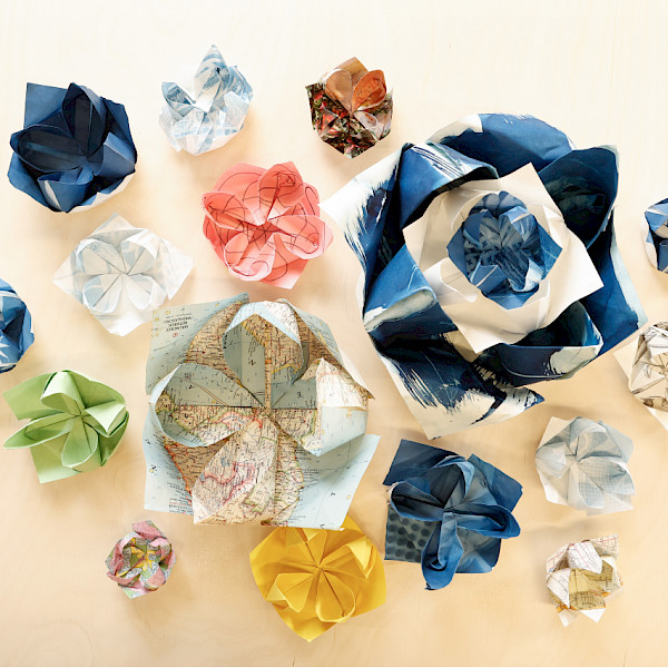 Photo of origami lotuses of various sizes and colors sitting on a light wooden table.