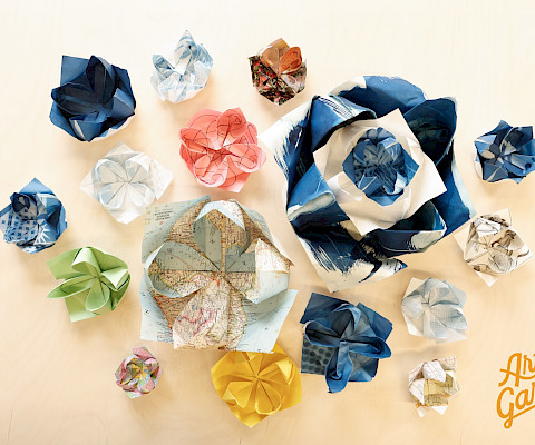 Photo of origami lotuses of various sizes and colors sitting on a light wooden table.