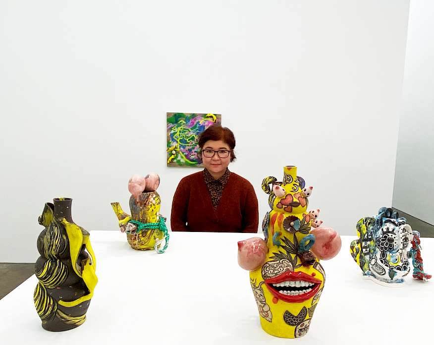 Photo of Jiha Moon standing in an art gallery next to a few of a her sculptures on a white platform.