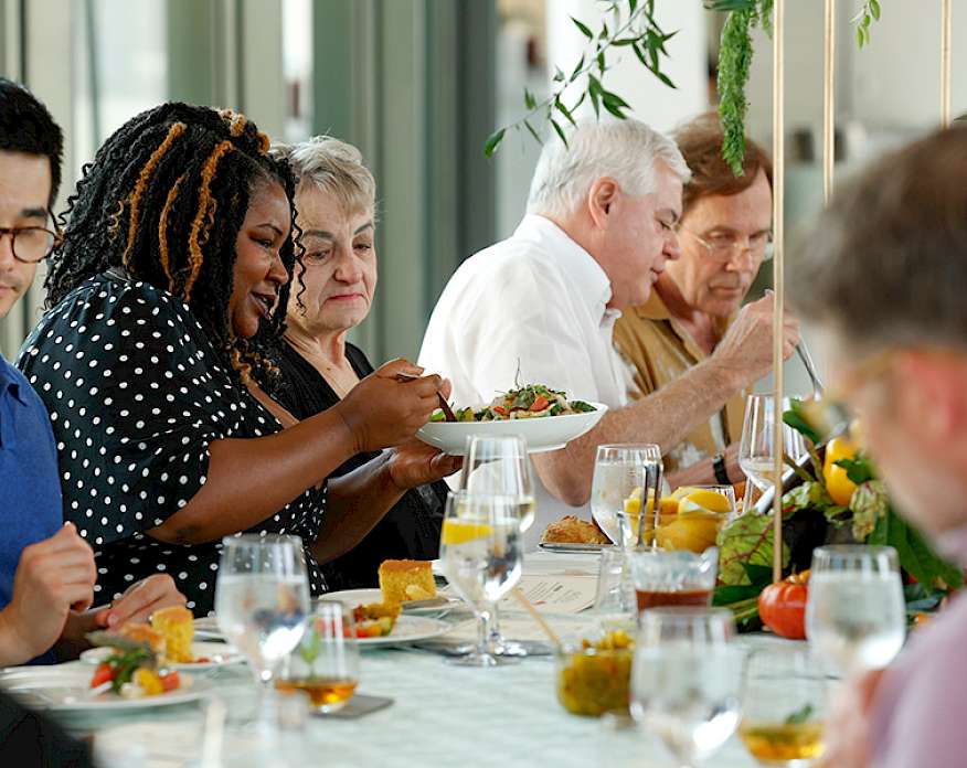 Photo of people sitting at a table and passing plates of food to each other.