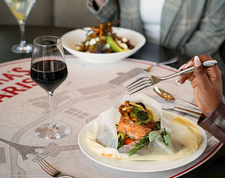 Close up photo of two plates of food on a table with two cocktails. The person in the foreground is holding a fork.