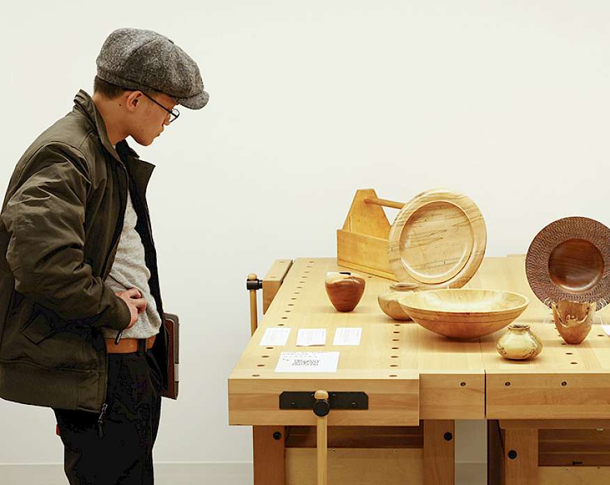 Photo of a man looking at handmade wooden vases and bowls on a table.