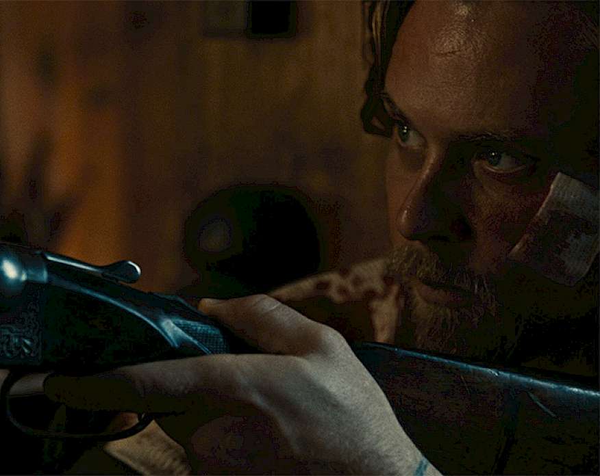 Film still from the movie Violet Ends showing a close up of a man with a bandaged face holding a rifle.