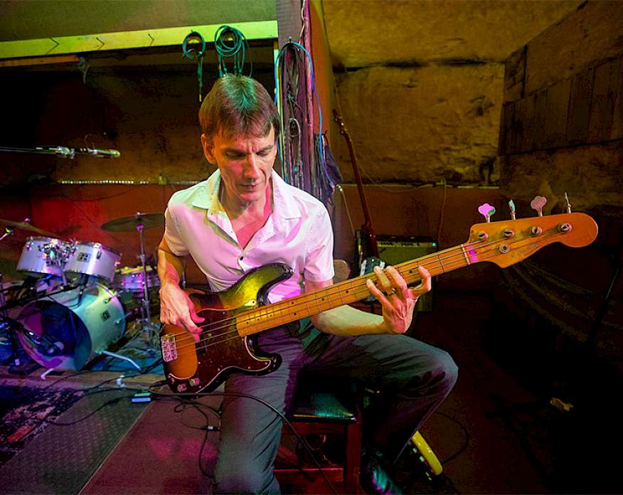 Photo of a man seated and playing an electric guitar.