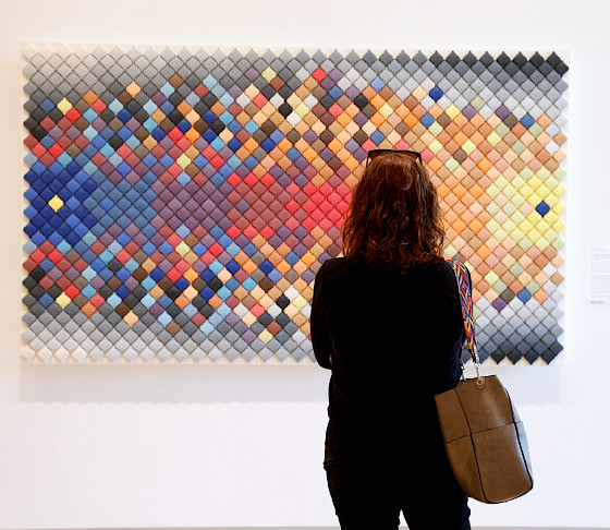 Photo of a woman looking at a work of art hanging on a wall.