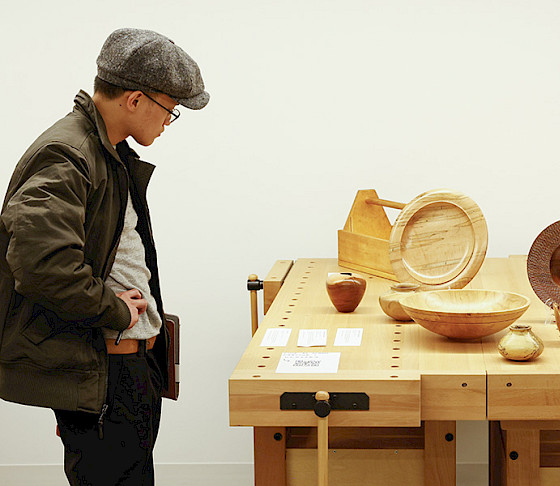 Photo of a man looking at handmade wooden vases and bowls on a table.