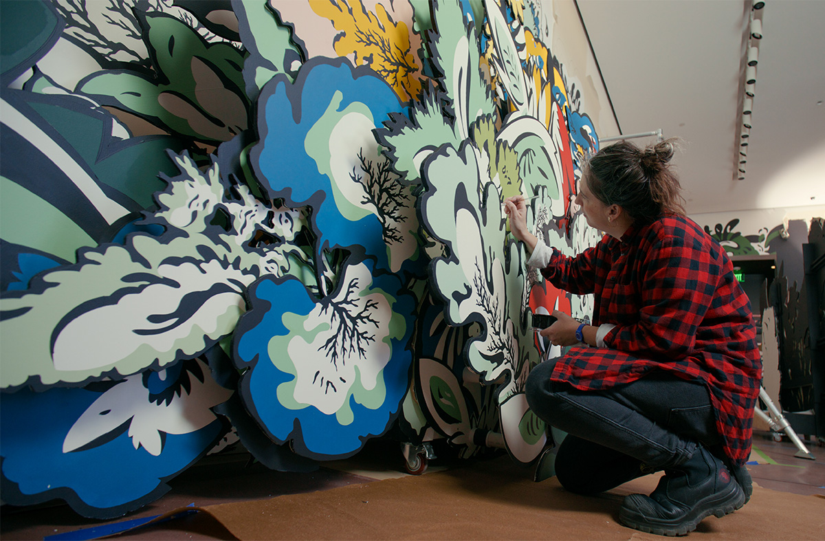 Still from a video of artist Natasha Bowdoin kneeling while painting an art installation.