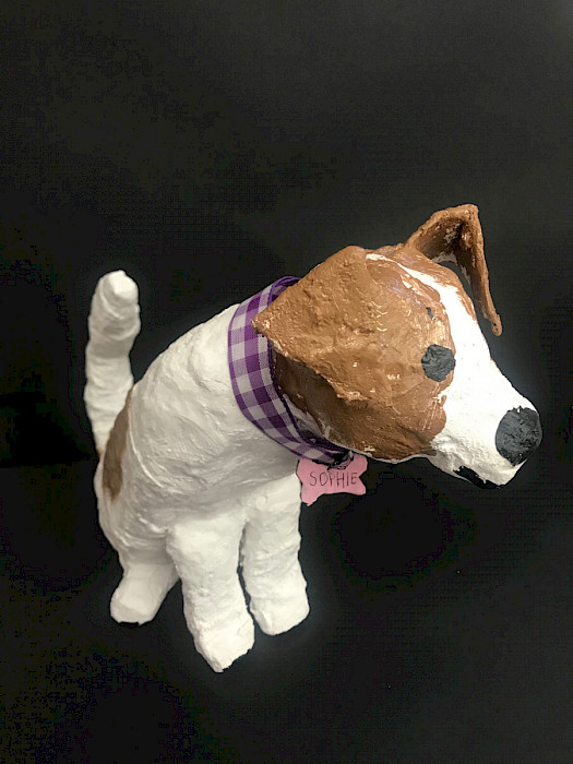 Photo of a paper mache sculpture depicting a brown and tie dog with a plaid purple collar and a pink name reading "Sophie."