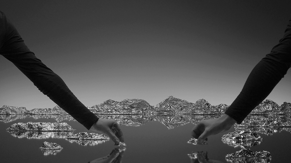 Film still depicting two hands placing rocks in a small set decorated with a lake.