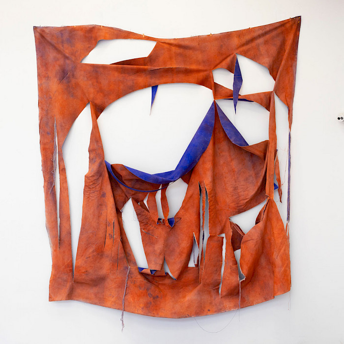 Photo of a large orange square of canvas torn in large sections to reveal a deep indigo paint on the opposite side hanging on a white wall.