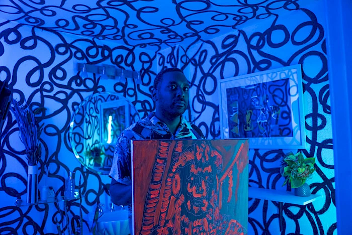 Film still of a man holding a painting on a canvas in a room with swirling black paint all over the walls.