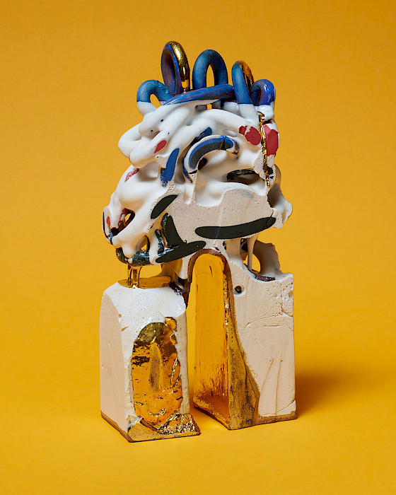 Photo of a white abstract ceramic sculpture with blue loops at the top and a tall gold arch and gold feet at the bottom.