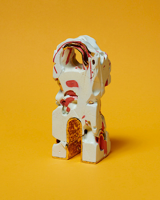 Photo of a white abstract ceramic sculpture with spots of pink glaze. It has a wide open arch on top and a narrow gold arch on bottom.