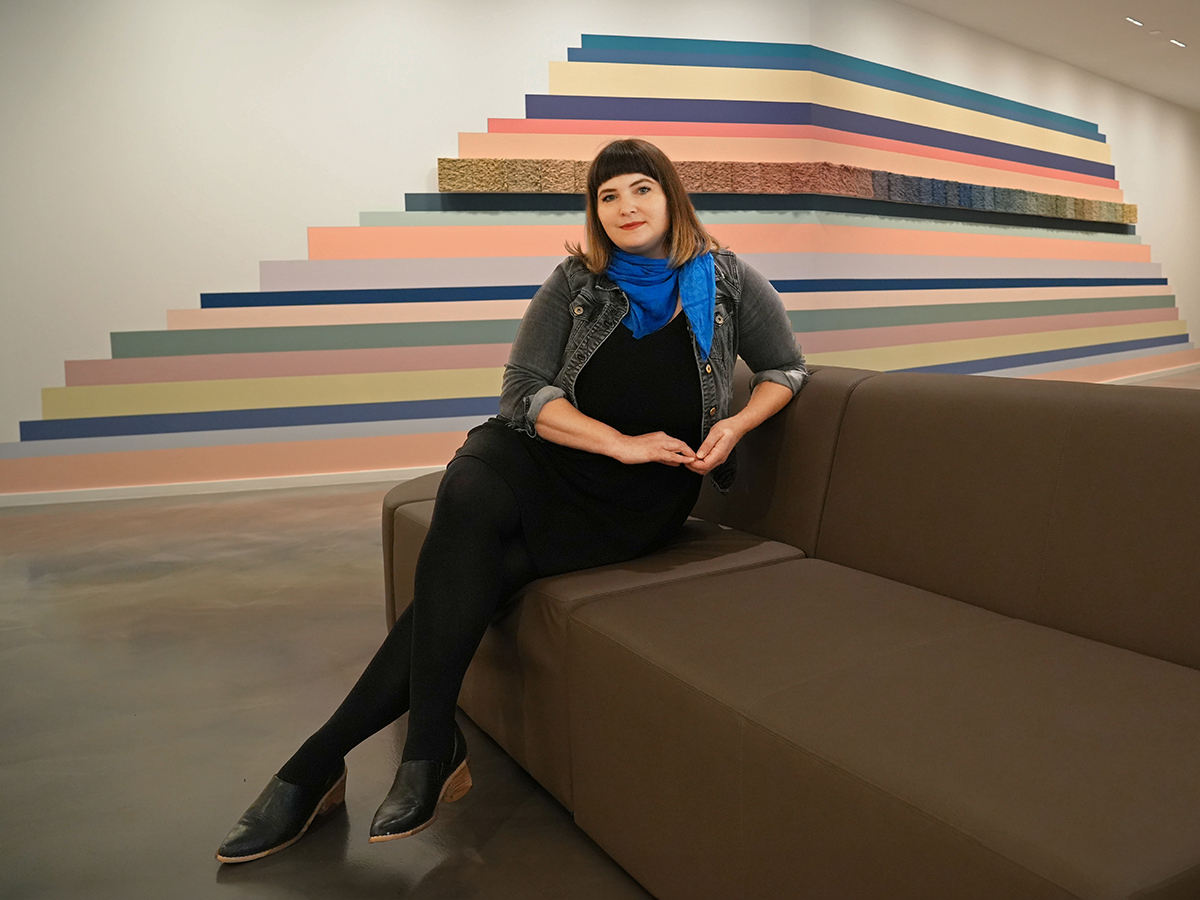 Photo of Risa Hricovsky sitting on a couch wearing a black dress and blue scarf.