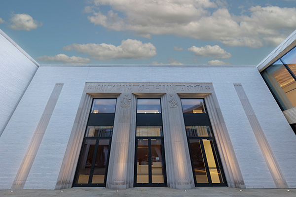 Photo of a white brick wall with carved stone entryways and tall glass doors.