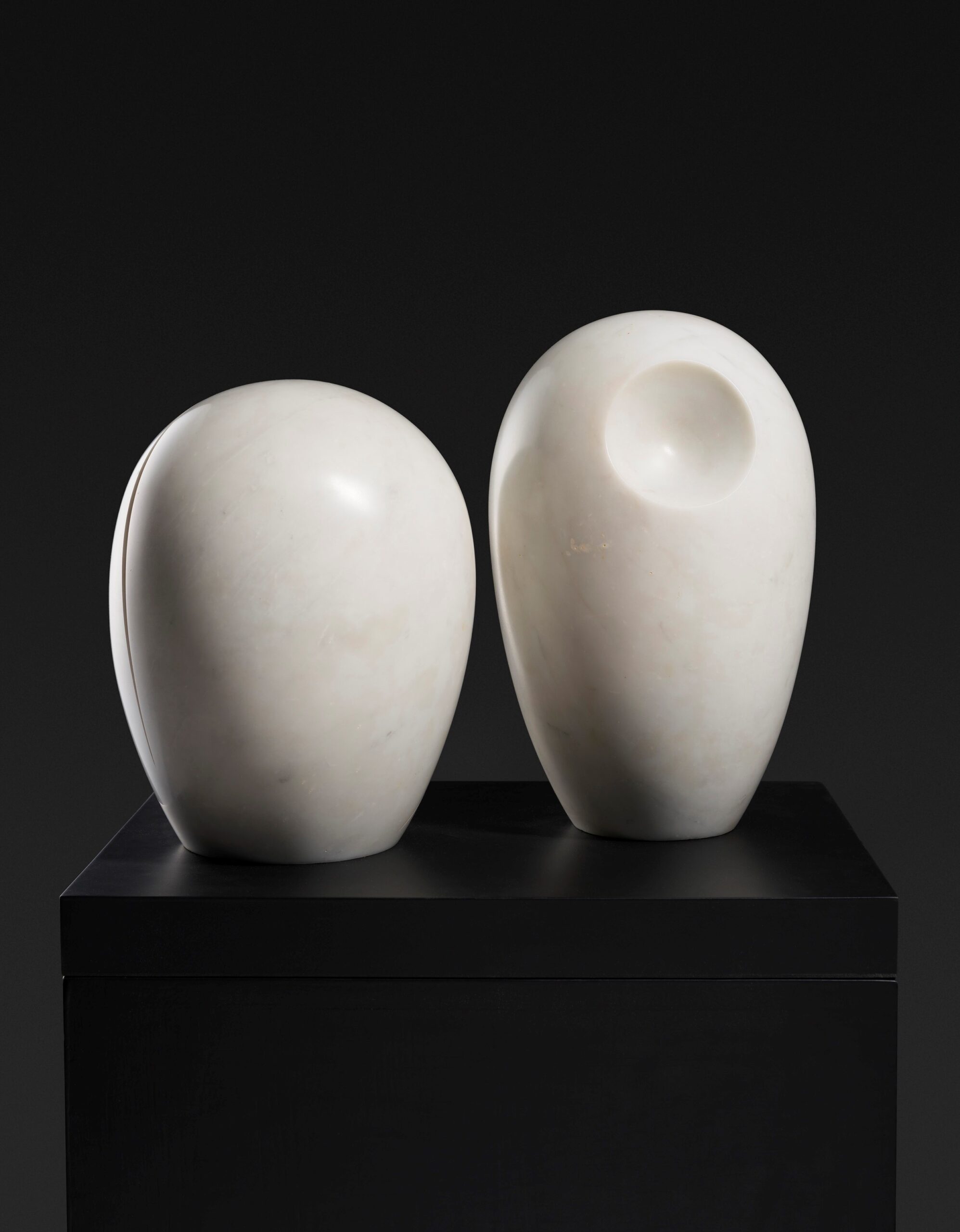 Photo of two white, egg-shaped marble sculptures. The sculpture on the right is slightly taller and has a semicircular concave top.