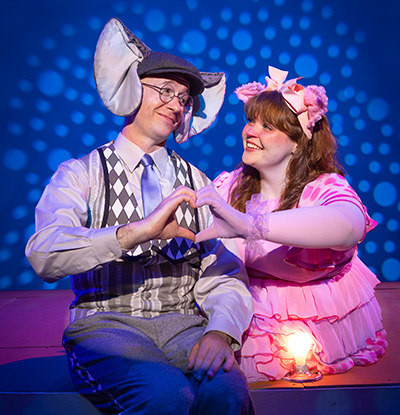 Photo of two actors dressed in character as Gerald the Elephant and Piggie the Pig sitting on a stage next a light bulb.