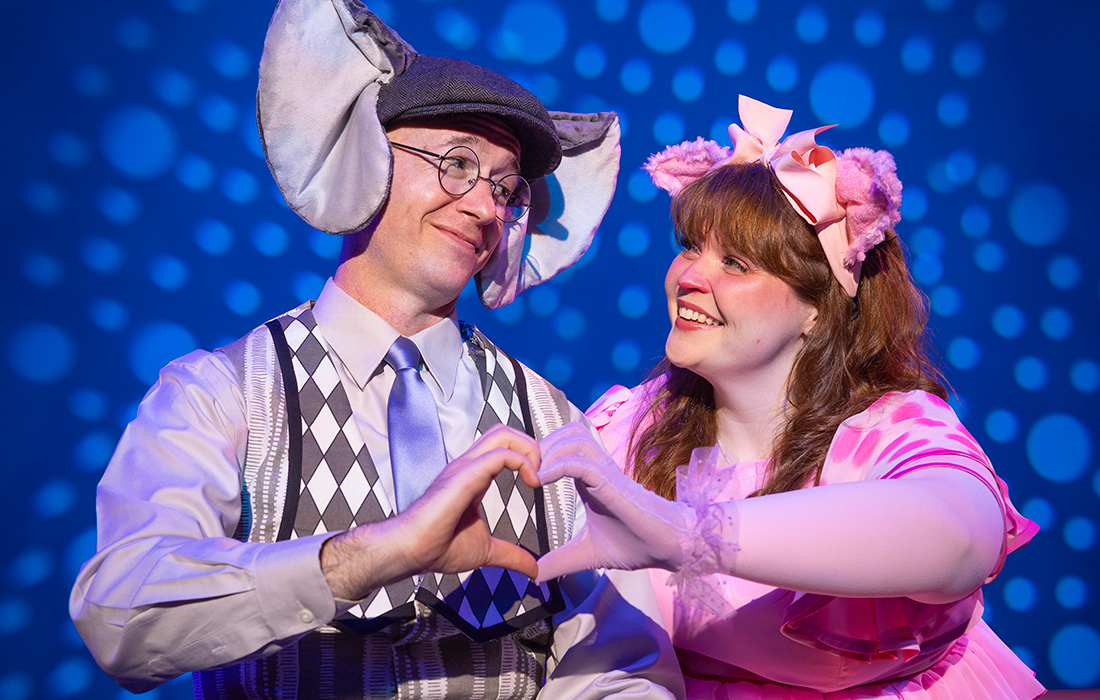 Photo of two actors dressed in character as Gerald the Elephant and Piggie the Pig sitting on a stage next a light bulb.