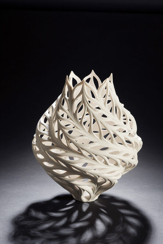 Photo of a sculpted white vase with an intricate cut-out pattern.