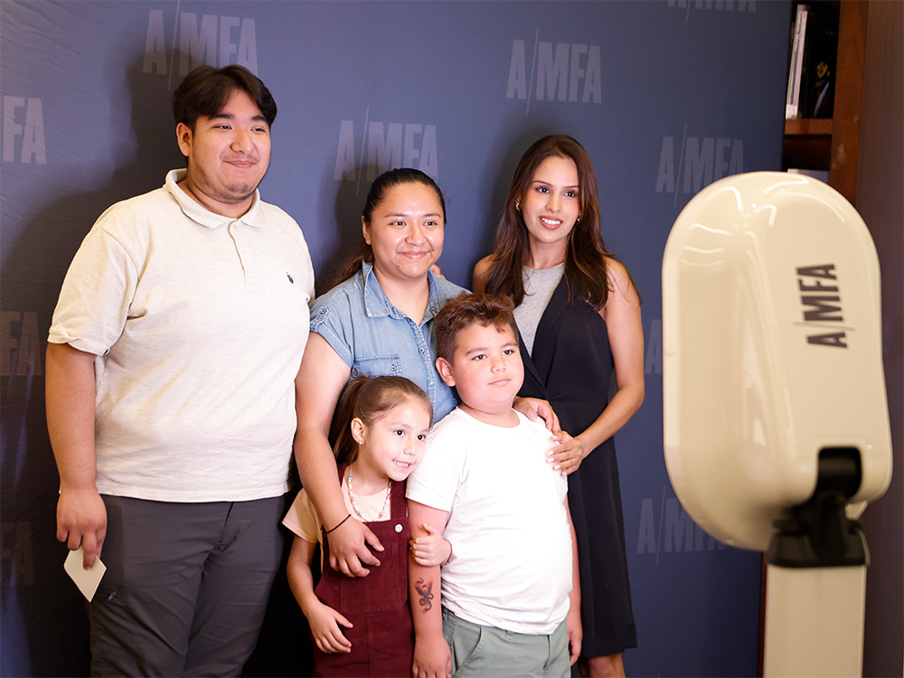 Photo of two women, a young man, and two young children smiling and posing in a photo booth with an AMFA logo background.