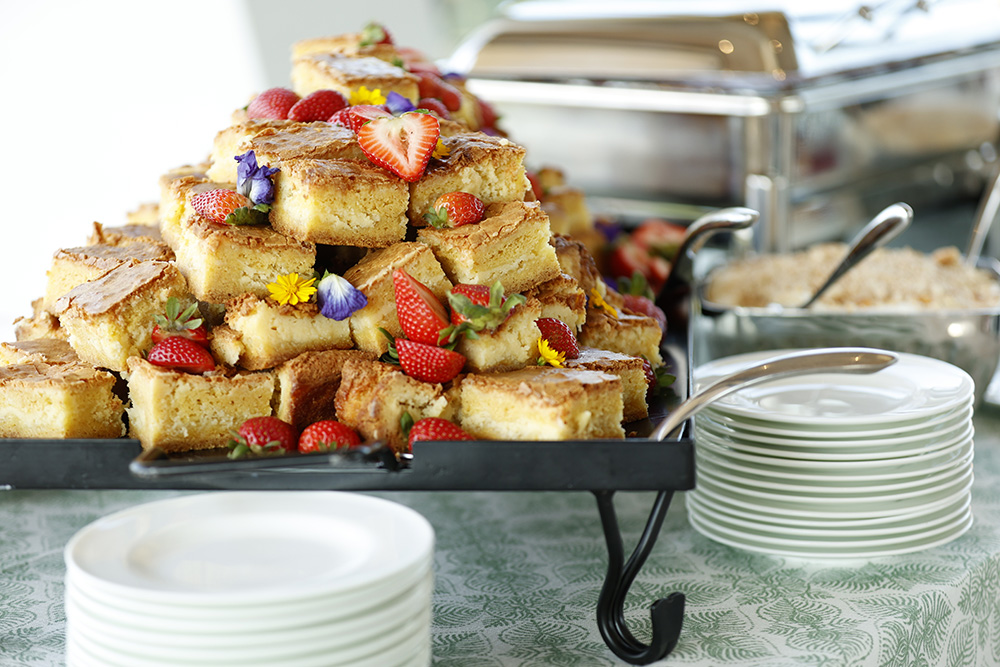 Photo of a platter of cornbread on a breakfast buffet next to a stack of plates.
