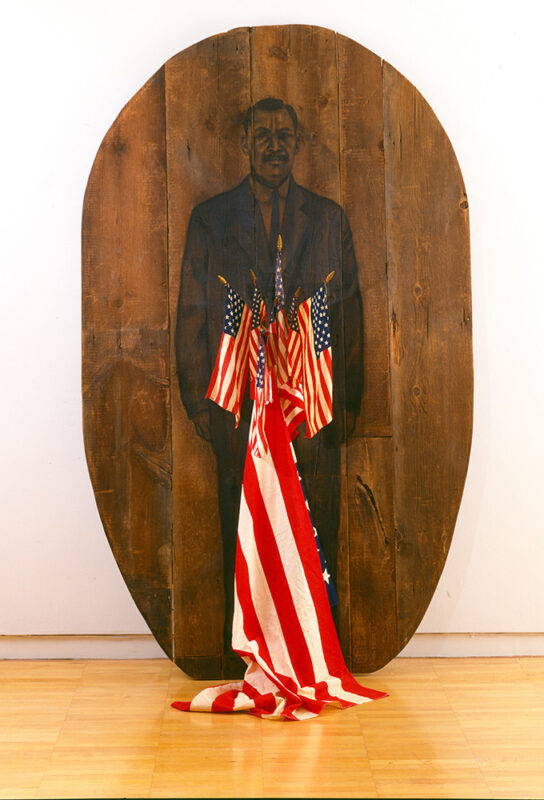 Photo of an large, oval-shaped wood slab adorned with a drawing of a man and several American flags.